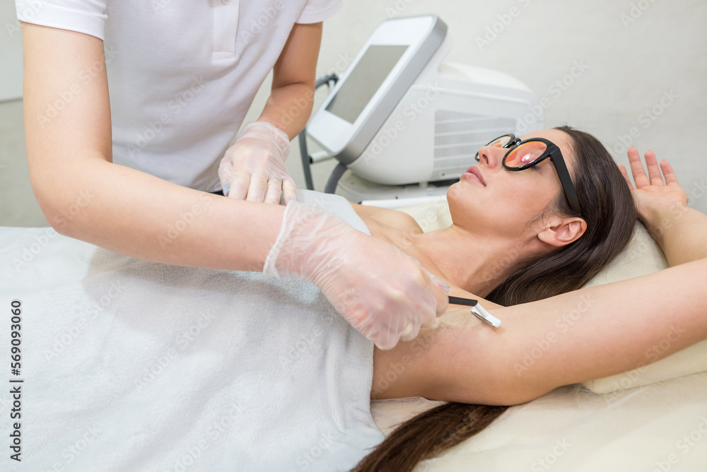 A woman beautician prepares her friend for laser hair removal. A woman beautician prepares her friend for laser hair removal.
