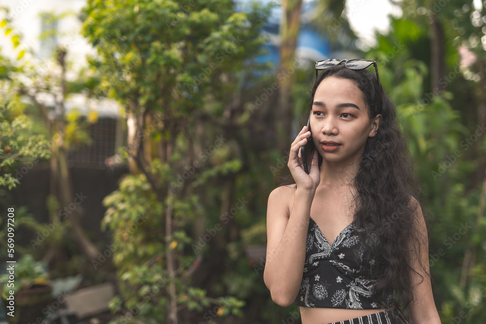 A pretty young Filipina woman with curly hair wearing a nice black top and long skirt talking on the phone at the garden. A pretty young Filipina woman with curly hair wearing a nice black top and long skirt talking on the phone at the garden.