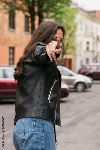 Sexy brunette in a leather jacket and jeans. A young woman poses for the camera against the background of a city street