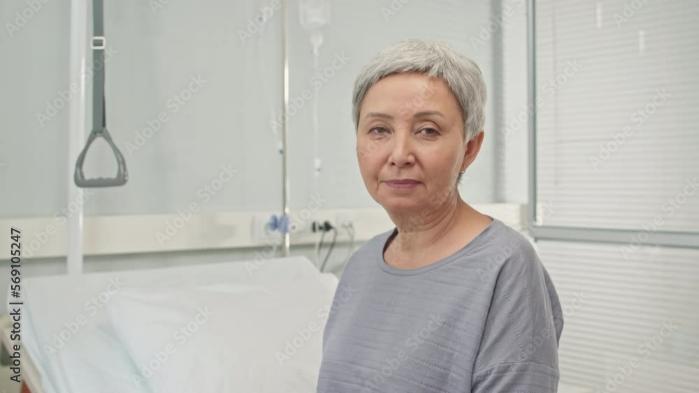 Portrait of senior Asian woman looking at camera sitting on bed in chamber in hospital Portrait of senior Asian woman looking at camera sitting on bed in chamber in hospital