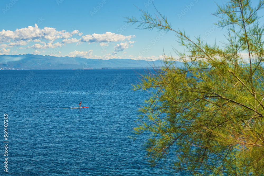 Fototapeta premium Unrecognizable person stand-up paddle boarding at Adriatic sea Kvarner gulf seen from the Lovran town coastline