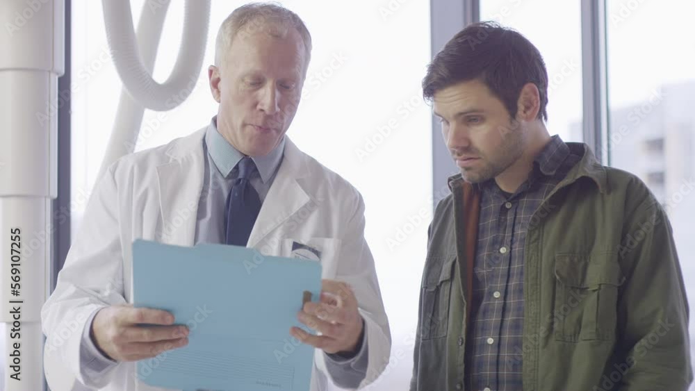 Handheld shot of male doctors discussing reports in hospital ward Handheld shot of male doctors discussing reports in hospital ward
