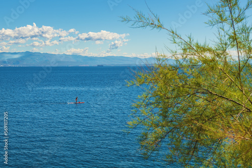 Unrecognizable person stand-up paddle boarding at Adriatic sea Kvarner gulf seen from the Lovran town coastline