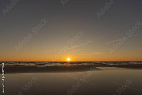 Sunset in a cloudless sky on the coast of the Gulf of Finland in Ust-Narva. The sky is clear, the waves gently roll on the sand. Estonia, Narva-Jyesuu. Natural background. Space for text.