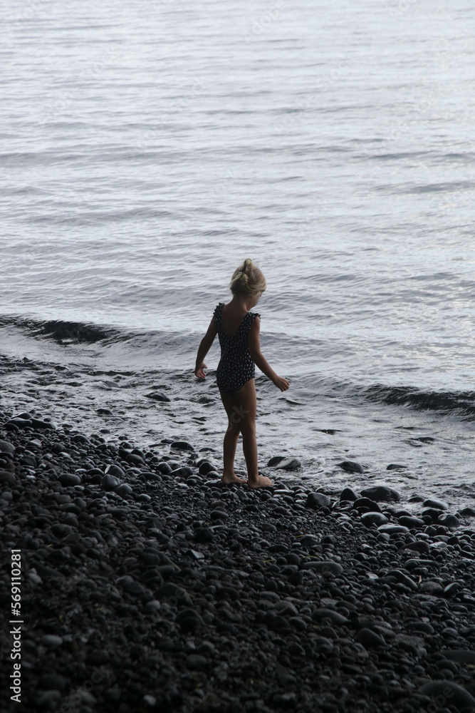 Adorable little girl on the huge empty black pebbled beach
