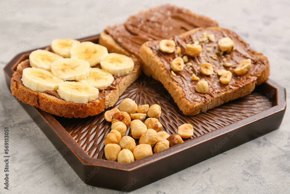 Wooden board of tasty toasts with hazelnut butter, banana and nuts on light background, closeup Wooden board of tasty toasts with hazelnut butter, banana and nuts on light background, closeup