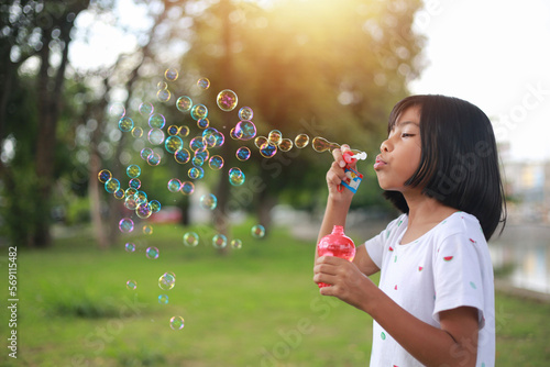 A little girl blowing soap bubbles in summer park.