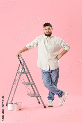Young man with ladder and cans of paint on pink background © Pixel-Shot