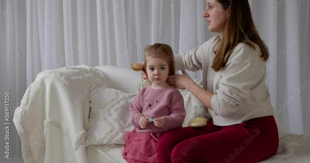 Loving mother sit sofa at home and combs hair of adorable daughter Loving mother sit sofa at home and combs hair of adorable daughter