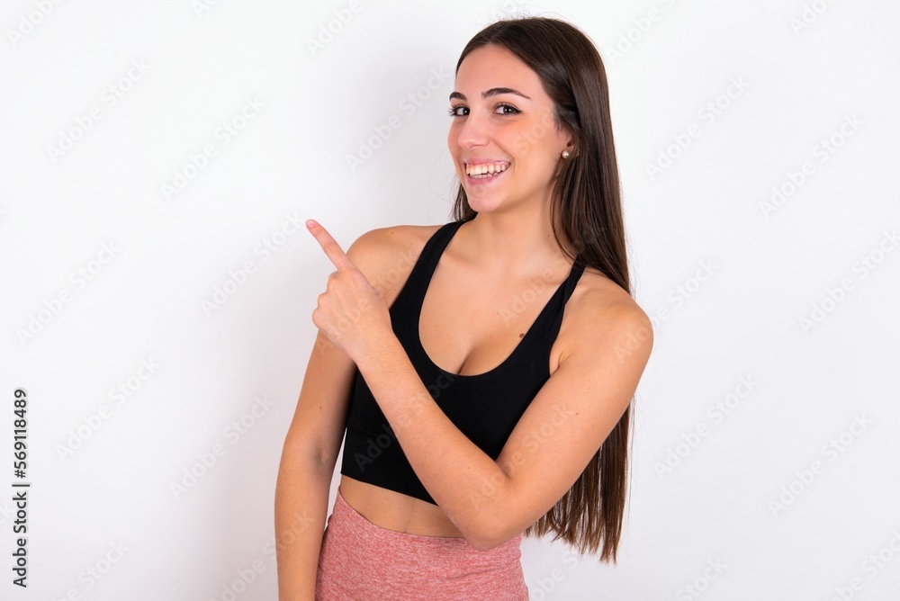 young woman wearing sportswear over white studio background pointing away and smiling to you. Look over there! young woman wearing sportswear over white studio background pointing away and smiling to you. Look over there!
