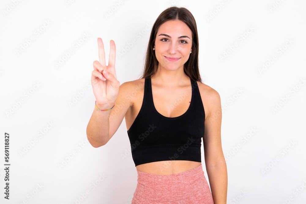 young woman wearing sportswear over white studio background showing and pointing up with fingers number two while smiling confident and happy. young woman wearing sportswear over white studio background showing and pointing up with fingers number two while smiling confident and happy.