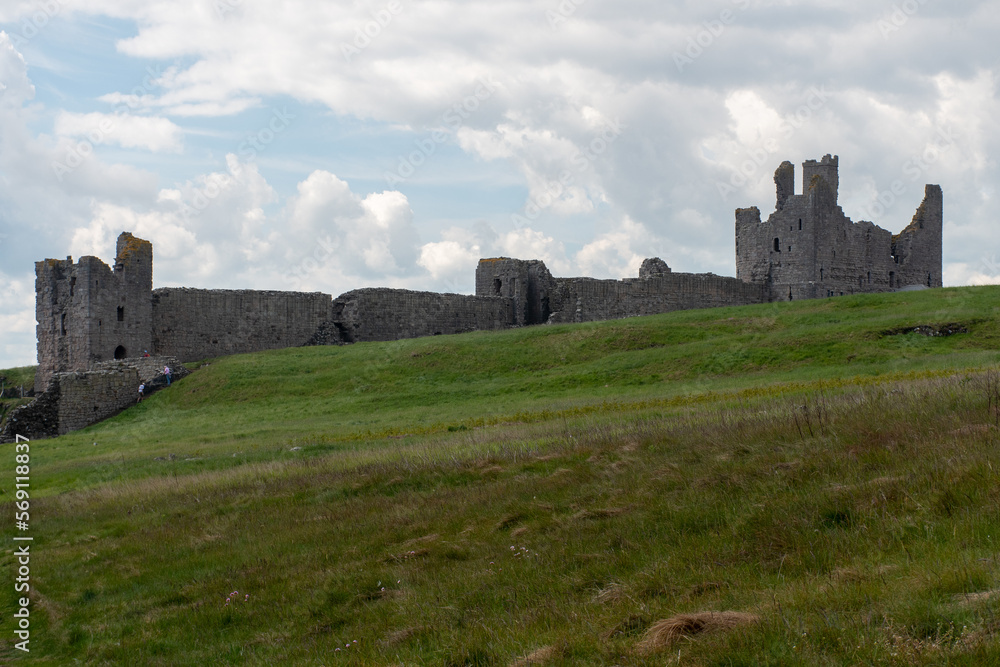 The ruins of Dunstanburgh Castle in Northumberland, with cloudy summer skies overhead