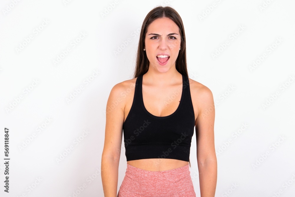 Stressful young woman wearing sportswear over white studio background screams in panic, closes eyes in terror, keeps hands on head, finds out terrified news, can't believe it. Stressful young woman wearing sportswear over white studio background screams in panic, closes eyes in terror, keeps hands on head, finds out terrified news, can't believe it.