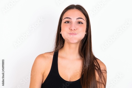 young woman wearing sportswear over white studio background puffing cheeks with funny face. Mouth inflated with air, crazy expression.