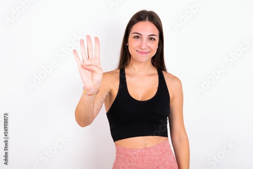 young woman wearing sportswear over white studio background showing and pointing up with fingers number four while smiling confident and happy. © Jihan