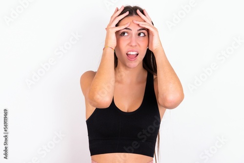Horrible, stress, shock. Portrait emotional crazy young woman wearing sportswear over white studio background clasping head in hands. Emotions, facial expression concept.