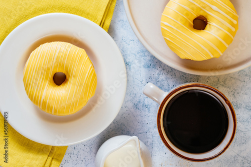 lemon doughnut in yellow glaze, coffee in a glass. 