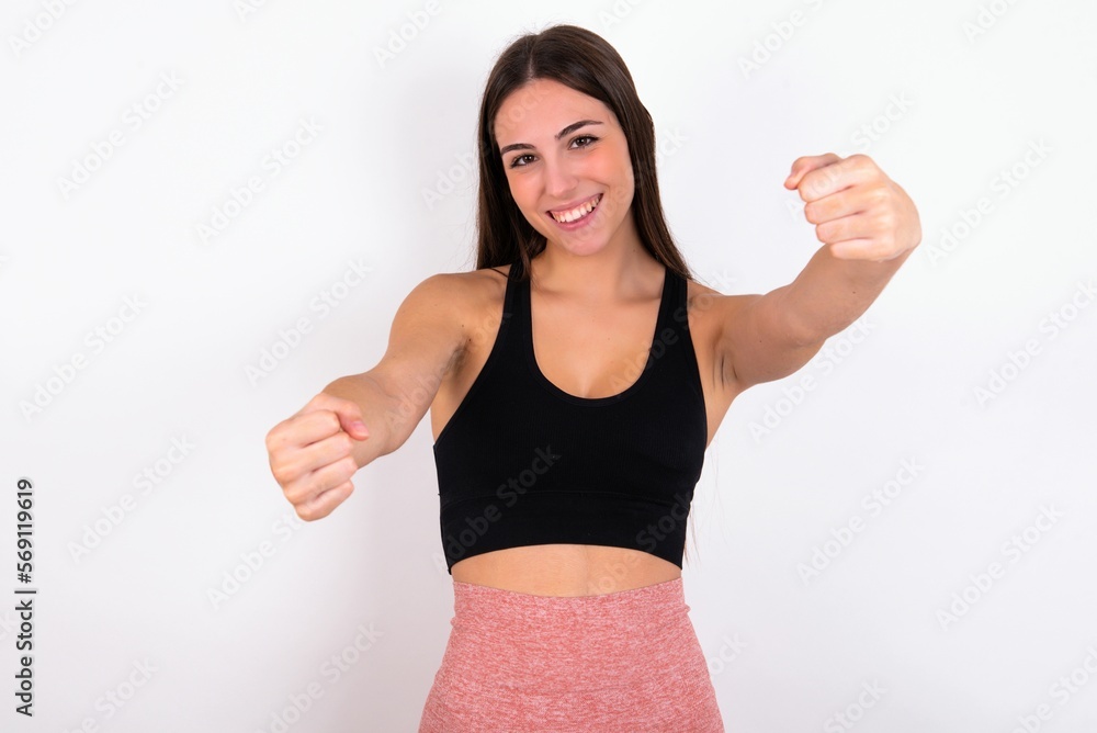 Portrait of charming young woman wearing sportswear over white studio background, smiling broadly while holding hands over her head. Confidence and relax concept. Portrait of charming young woman wearing sportswear over white studio background, smiling broadly while holding hands over her head. Confidence and relax concept.