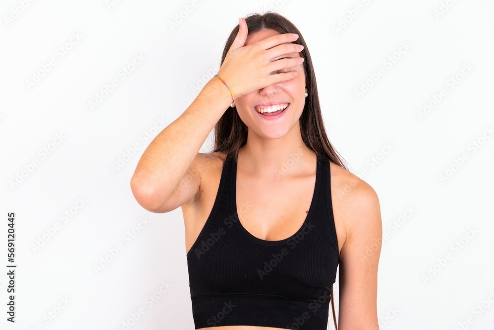 Happy young woman wearing sportswear over white studio background closing eyes with hand going to see surprise prepared by friend standing and smiling in anticipation for something wonderful. Happy young woman wearing sportswear over white studio background closing eyes with hand going to see surprise prepared by friend standing and smiling in anticipation for something wonderful.