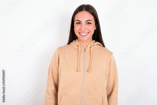 young woman wearing beige sweater over white studio background with nice beaming smile pleased expression. Positive emotions concept