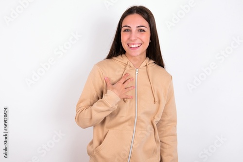 young woman wearing beige sweater over white studio background smiles toothily cannot believe eyes expresses good emotions and surprisement photo