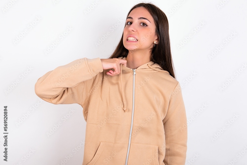 young woman wearing beige sweater over white studio background stressed, anxious, tired and frustrated, pulling shirt neck, looking frustrated with problem young woman wearing beige sweater over white studio background stressed, anxious, tired and frustrated, pulling shirt neck, looking frustrated with problem