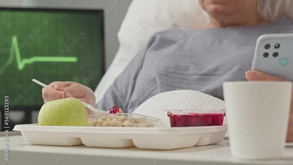 Cropped shot of unrecognizable female patient with smartphone having healthy breakfast in hospital bed Cropped shot of unrecognizable female patient with smartphone having healthy breakfast in hospital bed