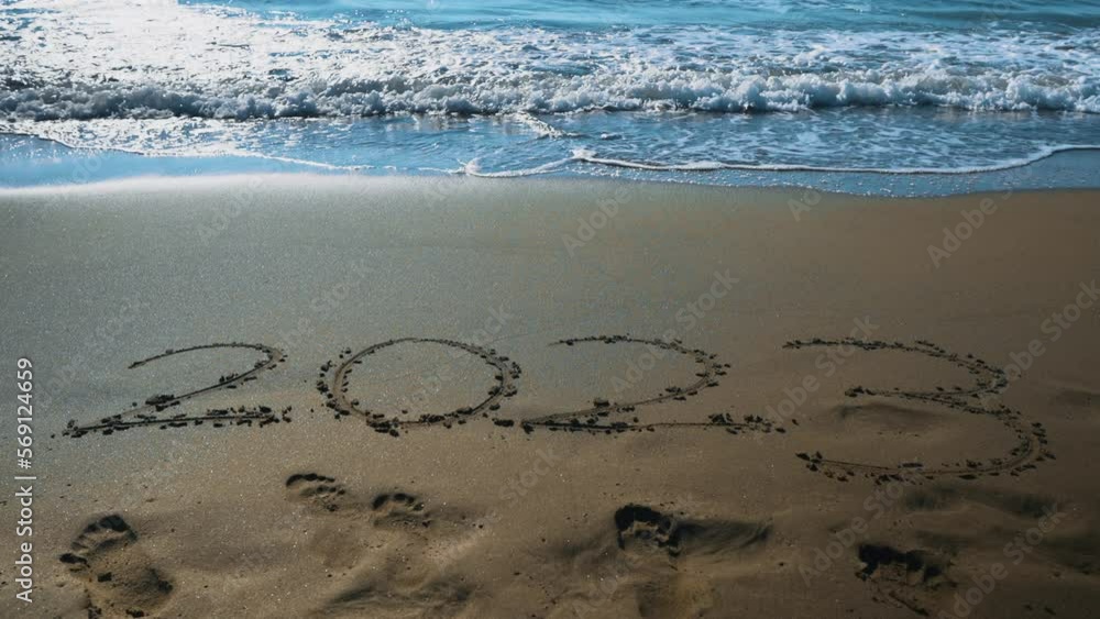 Year 2023 handwriting on sand beach surface.
