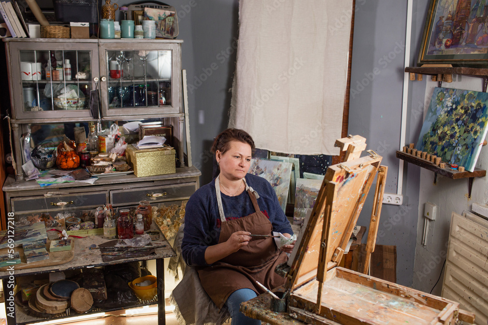 a professional female artist is engaged in painting on canvas in the studio. The artist paints a picture in her studio a professional female artist is engaged in painting on canvas in the studio. The artist paints a picture in her studio