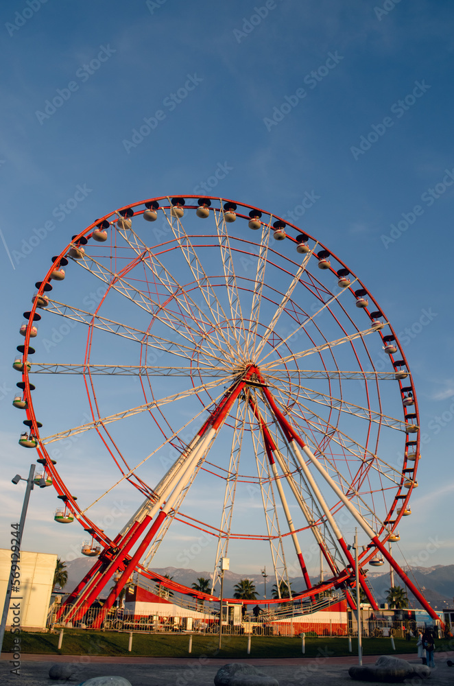 Attraction ferris wheel in the city, mountains and blue sky, vertical
