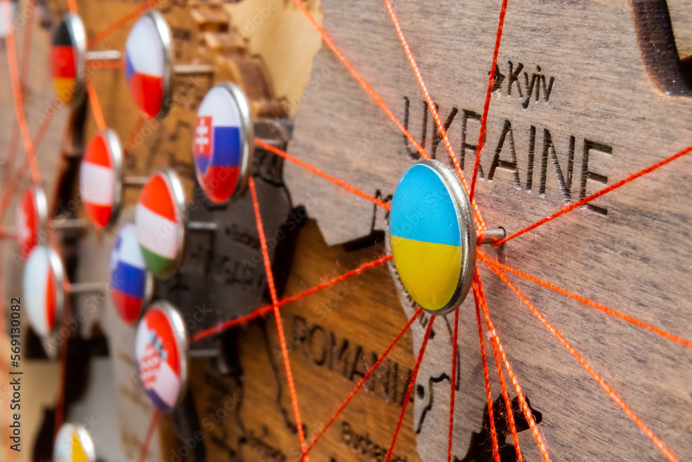 Ukraine flag on the pushpin and red threads on the wooden map connected with Europe. Travel or logistic routes. Influence in geopolitics and world economy. 