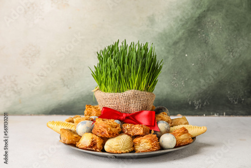 Plate with treats, eggs and grass on table near grunge wall. Novruz Bayram celebration