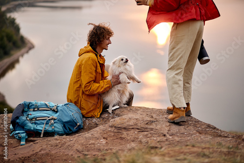 active couple with pet dog travelling in countryside, friendly family exploring wild nature, enjoy rest together. nice caucasian man and woman with backpacks exploring new places with cute spitz dog