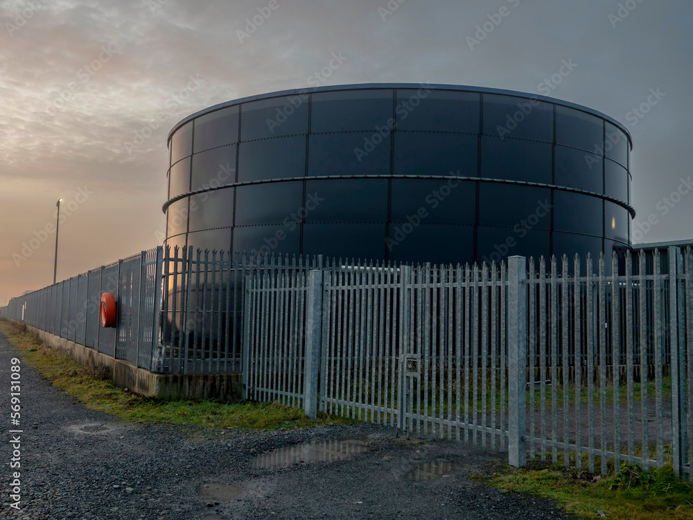 Tank for diesel or petrol fuel storage behind metal security fence at sunset. Oil industry supply chain. Protection of asset concept.