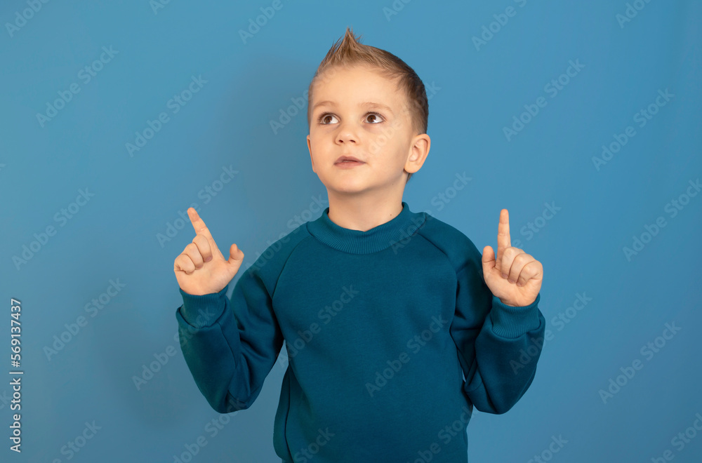 Happy boy in blue suit on blue background. Hand points to an empty space, cool sentence. demonstrating tips for solving space copying Happy boy in blue suit on blue background. Hand points to an empty space, cool sentence. demonstrating tips for solving space copying
