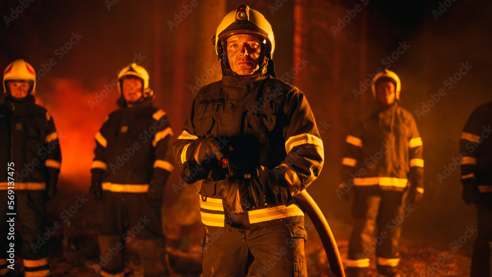 Portrait of a Brave Handsome Crew Leader in Safety Uniform and a Helmet Posing for Camera with Firefighters During a Wildfire. Professional Fireman Holding a Firehose in His Arms. Portrait of a Brave Handsome Crew Leader in Safety Uniform and a Helmet Posing for Camera with Firefighters During a Wildfire. Professional Fireman Holding a Firehose in His Arms.