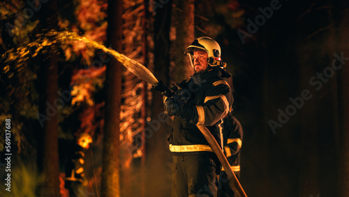 Experienced Firefighter Extinguishing a Wildland Fire Deep in a Smoke-Filled Forest. Professional in Safety Uniform and Helmet Using a Firehose to Battle Dangerous Fire. © Gorodenkoff