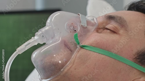 Closeup of man breathing through oxygen mask while lying on hospital bed