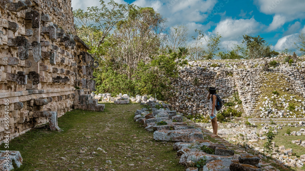 Woman standing and looking at the sculptures of Uxma, old maya temple in Yucatan Woman standing and looking at the sculptures of Uxma, old maya temple in Yucatan