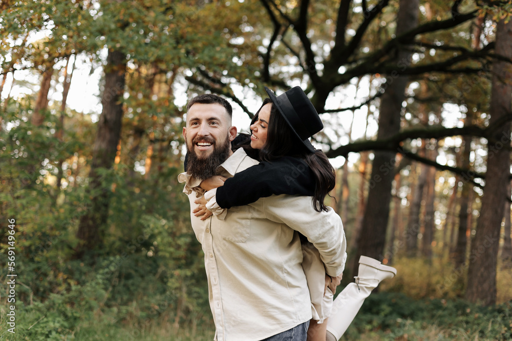Valentines day. Happy young bearded man piggybacking his girlfriend. Loving stylish couple having fun on date in nature outdoors. Heterosexual couple are embracing in the park on warm day. Valentines day. Happy young bearded man piggybacking his girlfriend. Loving stylish couple having fun on date in nature outdoors. Heterosexual couple are embracing in the park on warm day.