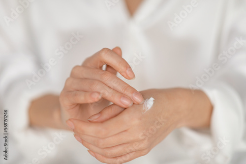 Caucasian millennial female applying cream on hands, enjoy good morning in bedroom, close up, cropped