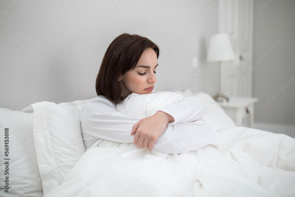 Lonely upset young woman sitting alone in bed