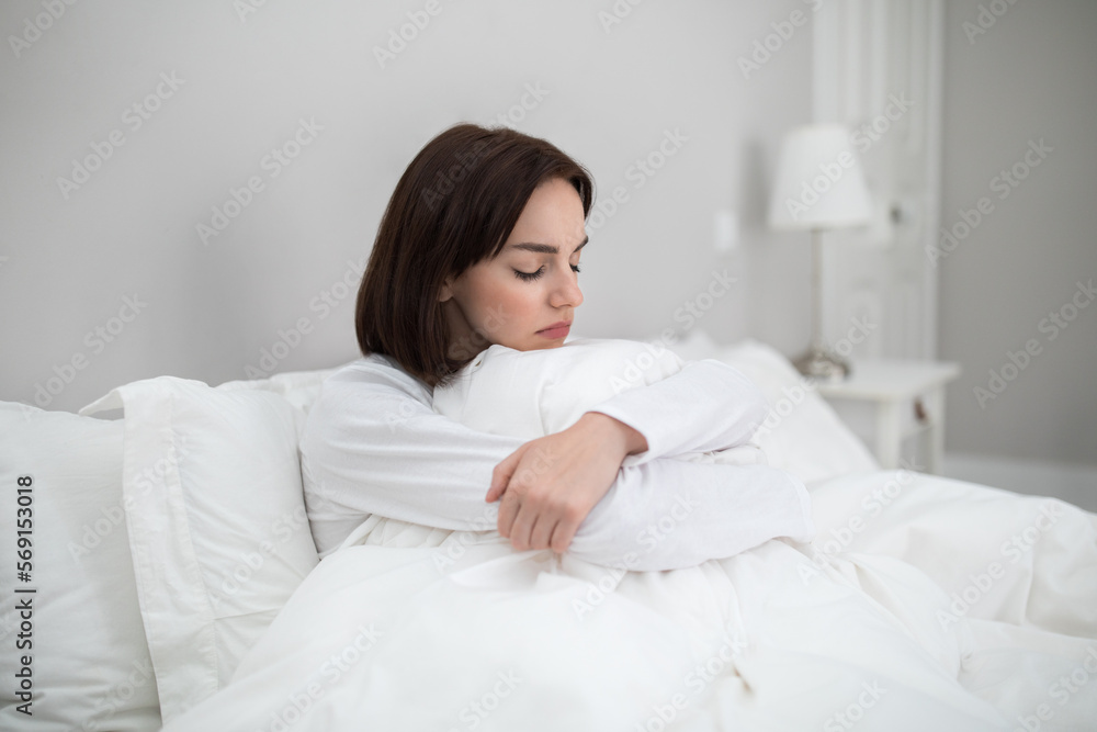 Lonely upset young woman sitting alone in bed Lonely upset young woman sitting alone in bed