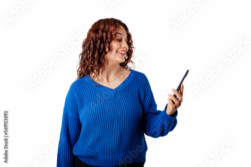 Young woman smiling confident wearing knitted sweater standing isolated over white background looking at the phone screen, celebrating an online win, overjoyed. Using mobile phone make winner gesture.