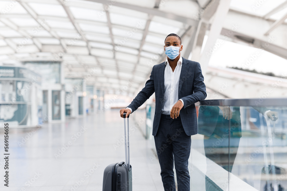 Travel Safety. Portrait Of Black Businessman In Medical Mask Standing In Airport Travel Safety. Portrait Of Black Businessman In Medical Mask Standing In Airport