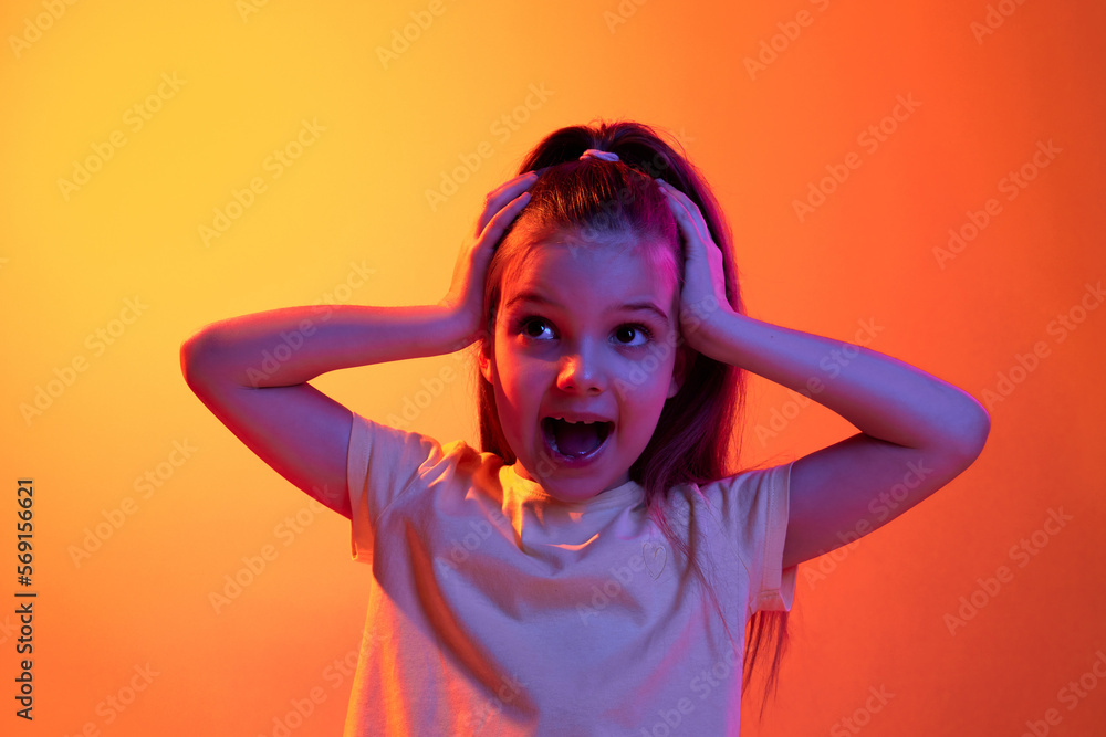 Positive shock. Portrait of little girl, child posing with emotional face over gradient orange background in neon light. Concept of childhood, emotions, fashion, lifestyle, facial expression Positive shock. Portrait of little girl, child posing with emotional face over gradient orange background in neon light. Concept of childhood, emotions, fashion, lifestyle, facial expression
