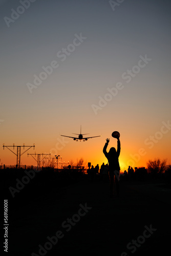 A backlit woman raises her arms to airplanes at sunset as a sign of travel and adventure.