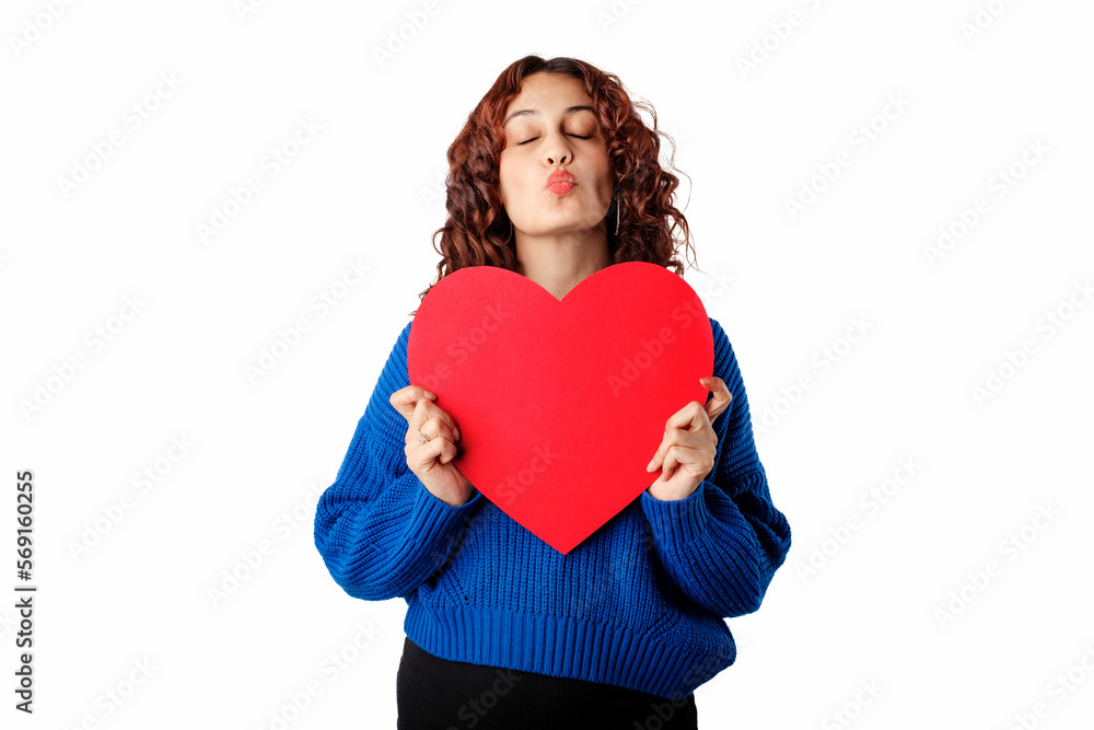 Young woman smiling confident standing isolated over white background puckering lips in a kiss, poses with a large cardboard heart shape in hand. Eyes are closed, thinking of lover. Young woman smiling confident standing isolated over white background puckering lips in a kiss, poses with a large cardboard heart shape in hand. Eyes are closed, thinking of lover.