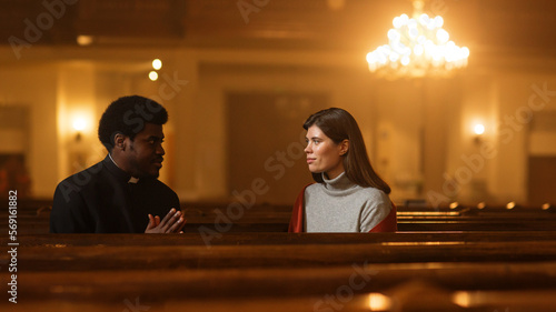 Talk in Church: The Pastor's Gentle Voice Brings Comfort and Solace To Young Female Parishioner. With Gentle Words of Reassurance He Reminds Woman of the Power of Christian Faith and the Love of God photo