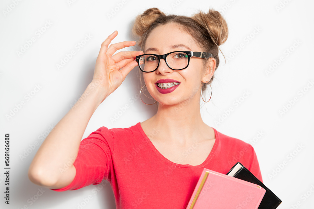 the portrait of young blondie caucasian woman with two hair bundles, glasses for vision, braces smiling widely and holding some notebooks; young woman businessman concept the portrait of young blondie caucasian woman with two hair bundles, glasses for vision, braces smiling widely and holding some notebooks; young woman businessman concept